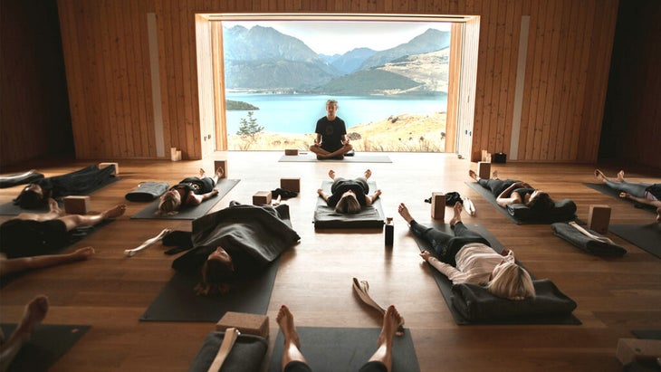 a class of yoga students at a wellness retreat laying in Savasana in front of a large window facing a lake.