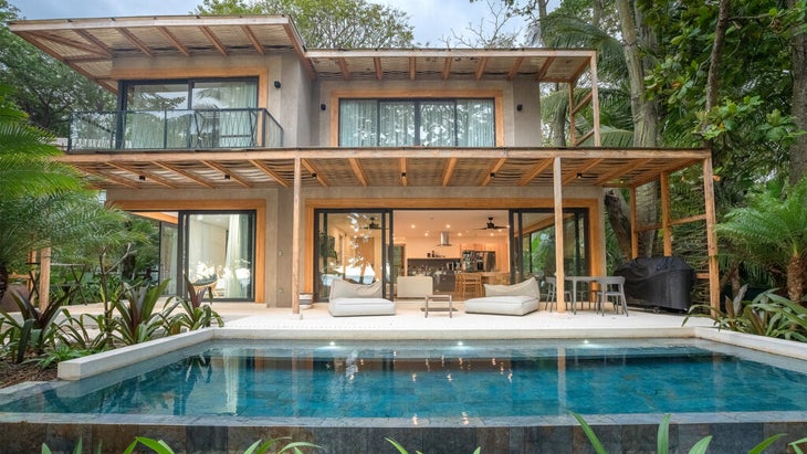 A poolside bungalow with open windows at a wellness resort surrounded by tropical trees