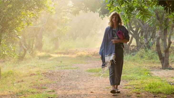 woman walking through a grove of trees with a pink yoga mat rolled under her arm at a wellness retreat